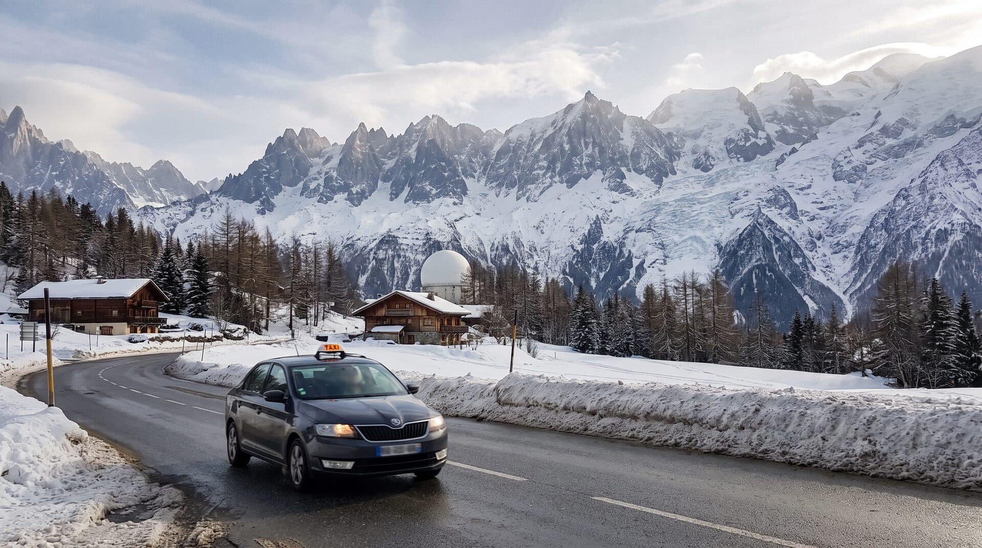 Un taxi sur la route de la vallée de Chamonix, chalets et massif du Mont-Blanc enneigé en arrière-plan